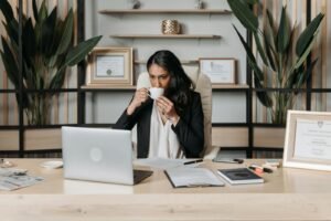 Woman sipping coffee while working on a laptop in a modern office.