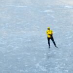 2 person in yellow jacket and black pants walking on snow covered ground during daytime